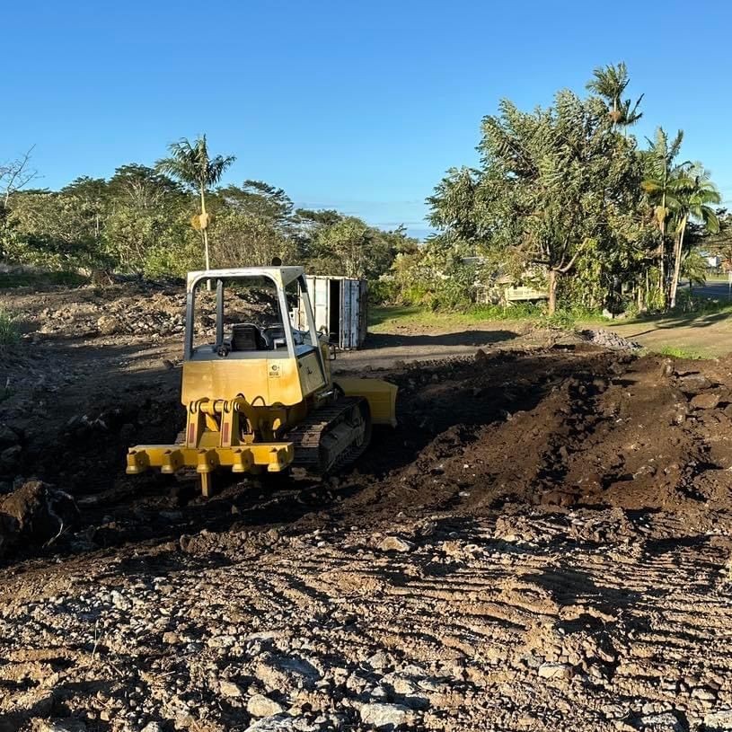 Yellow bulldozer moving soil on a construction site with trees and clear sky in the background.