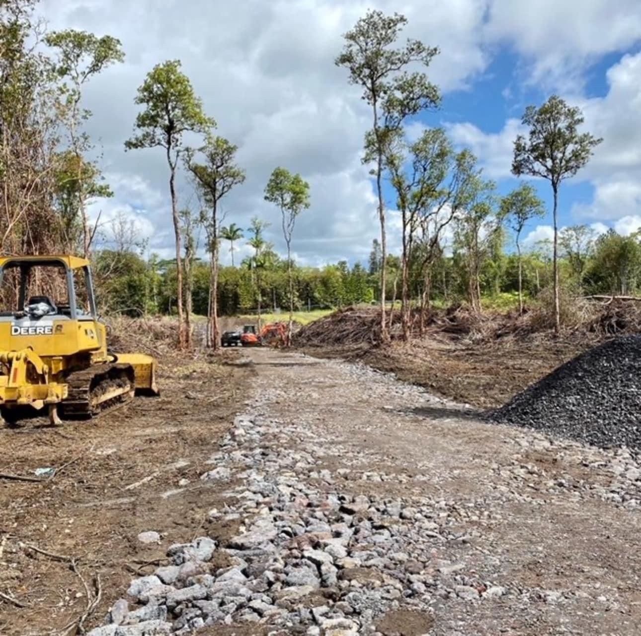 Construction site with bulldozer on a partially cleared forest area, under a cloudy sky.